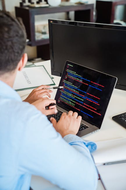 A close-up view of a silver laptop with a white keyboard displaying a software development environment. The screen shows lines of code in a text editor on the left side, with syntax highlighting, and 